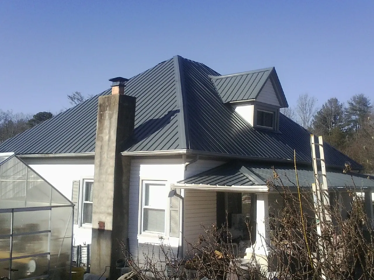 Dark blue standing seam metal roof on a white farmhouse with dormer — Slate & Tile Roof Repair by Roofing Brothers in Mcclellan