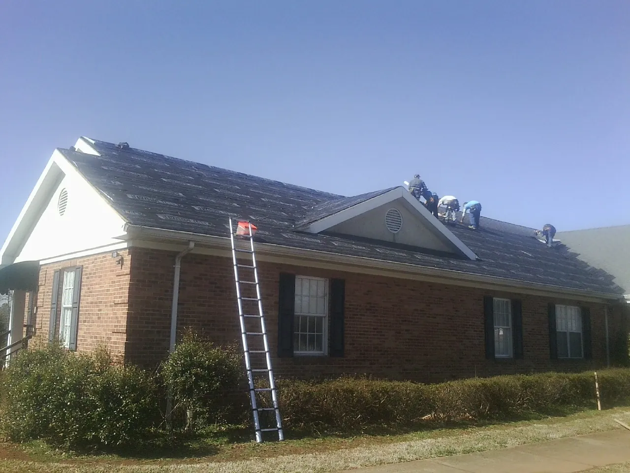 Crew tearing shingles off a brick ranch roof with a ladder set — Metal Roof Repair work by our crew in Mcclellan