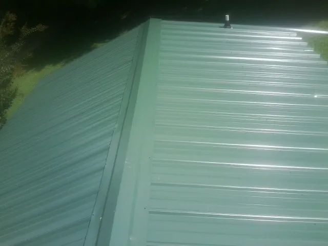 New green metal panels meeting at the ridge of a roof — Flat Roof Repair work by our crew in Mcclellan