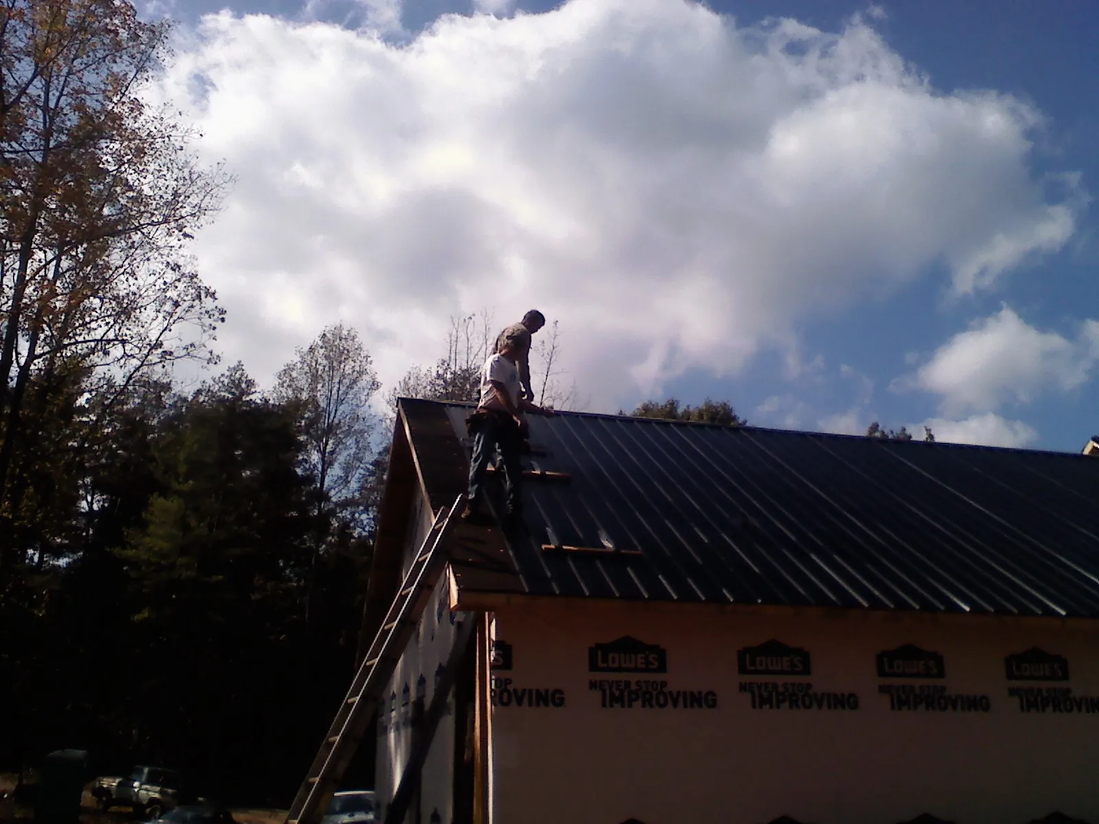 Roofer fastening dark metal panels high against a cloudy sky, from a Roof Inspection job in Mcclellan