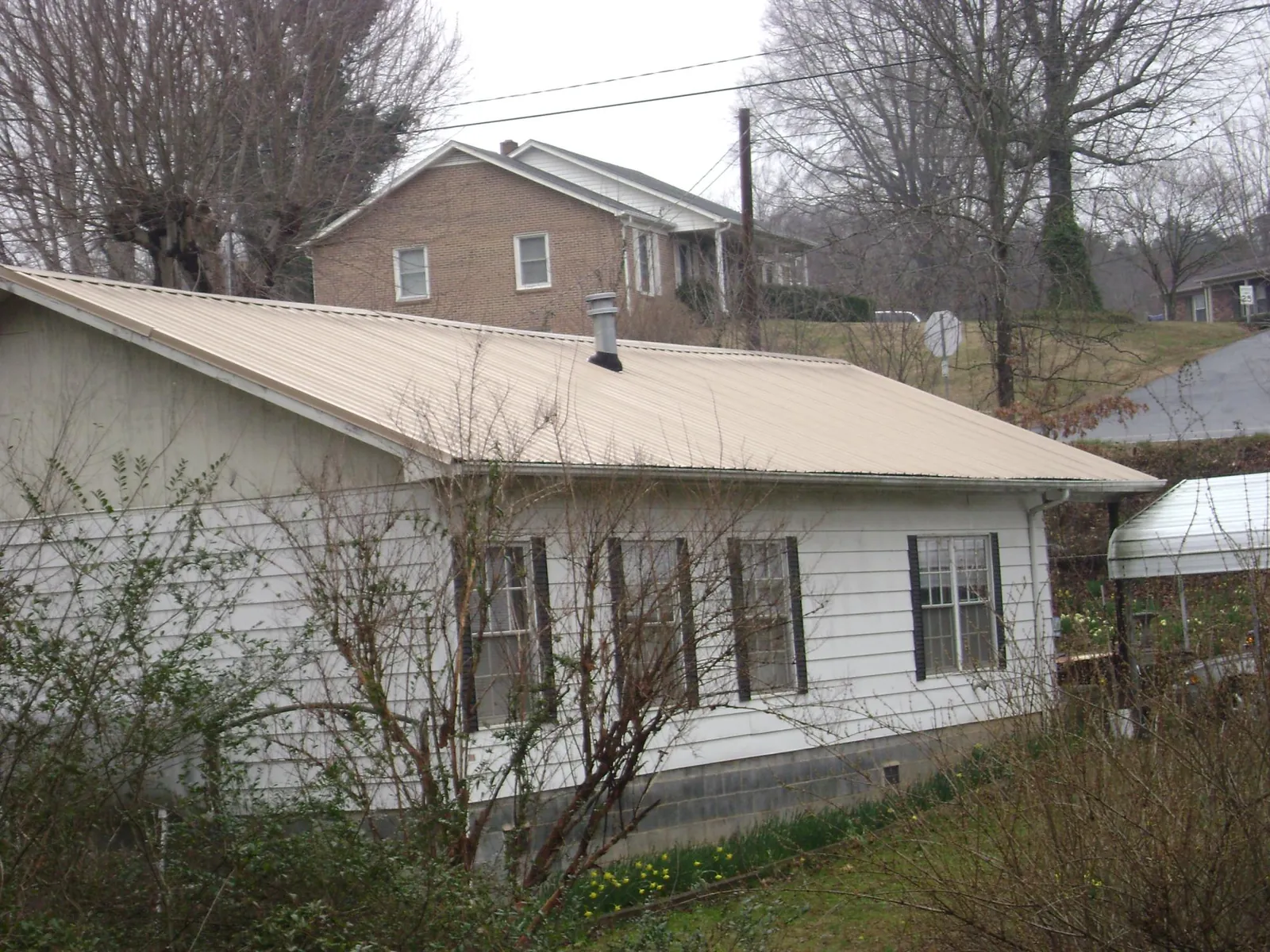 Tan metal roof on a white sided house set into a hillside — Commercial Roofing by Roofing Brothers in Mcclellan